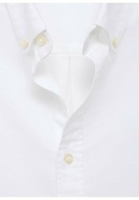 Camicia bianca con colletto a punta, dotata di due chiusure a bottone e un tessuto testurizzato. Il design interno è semplice e poco invadente.