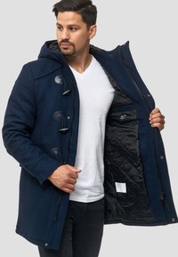 Abrigo de lana azul marino con capucha, que presenta botones tipo toggle, cierre de cremallera y un forro interior acolchado negro.