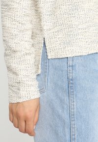 Svetlý texturovaný svetr s volnou vazbou, s dlouhými rukávy a postranními rozparky, kombinovaný s džíny s vysokým pasem.