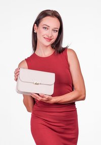 Béžová psaníčko s překlopným klopovým zapínáním, vyznačující se zlatým akcentem a texturovaným povrchem. Modelka má na sobě úzké červené šaty a drží psaníčko.