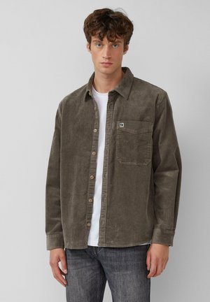 Bruine ribfluwelen shirt met verticale ribbels, knoopsluiting, borstzak en een klein logo. Draag dit over een wit T-shirt en combineer het met een grijze spijkerbroek.