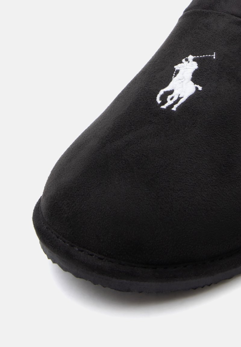 Slipper in suede nero con logo di un giocatore di polo ricamato in bianco sulla parte anteriore superiore e bordi in gomma nera visibili.