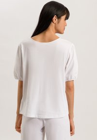 Top bianco a maniche corte con scollo arrotondato, dotato di maniche leggermente a sbuffo e una vestibilità ampia per il massimo comfort. Tessuto con una texture liscia.
