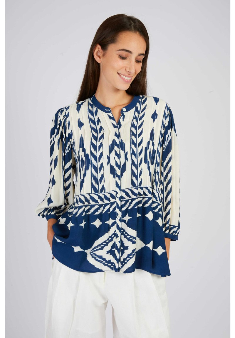 Blouse navy et écrue à motifs avec un col rond, une fermeture à boutons et des manches trois-quarts. Présente des motifs géométriques et rayés.