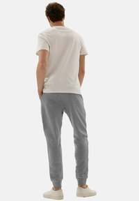 Męskie szare dresy z elastycznymi mankietami, o miękkiej fakturze i dwóch tylnych kieszeniach, zestawione z prostą białą koszulką z krótkim rękawem.