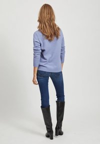 Jasnofioletowy sweter z prążkowanymi mankietami i dołem, w połączeniu z ciemnoniebieskimi dżinsami i czarnymi botkami do kolan. Gładka tekstura, luźny krój.