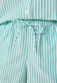 Lichte katoenen shorts in aqua en witte strepen. Heeft een gathered tailleband met een trekkoord en een knoopdetail bovenaan.