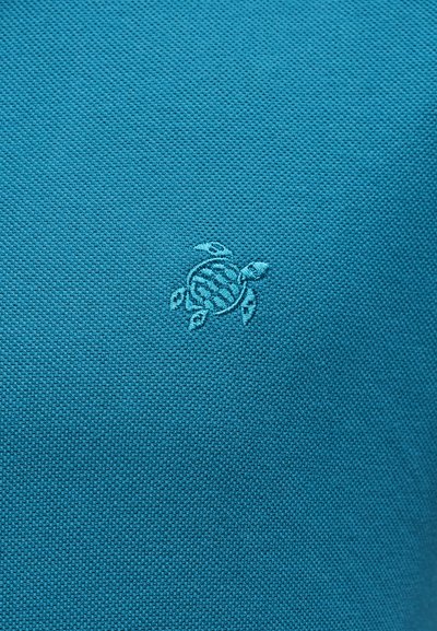Τουρκουάζ ύφασμα με μικρό κεντητό λογότυπο θαλάσσιας χελώνας σε νήμα που ταιριάζει, κεντραρισμένο στο πλαίσιο.