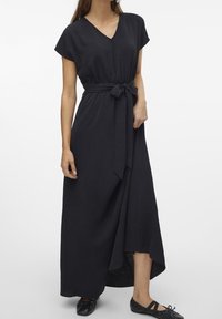 Svart maxiklänning med v-ringning, korta ärmar och midjeband. Har en texturerad tyg och en hög-låg fåll. Bärs med svarta ballerinaskor.