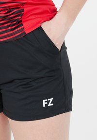 Svarta sportshorts med en slät textur, utrustade med en sidoficka och en vit "FZ"-logotyp på nederkanten. Designen är enkel och funktionell.