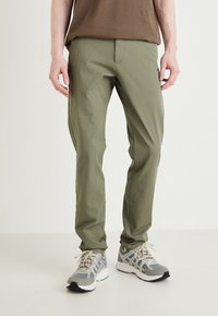 Pantaloni slim-fit verde oliva realizzati in tessuto leggero con una texture liscia. Caratterizzati da una vita a media altezza e tasche frontali.