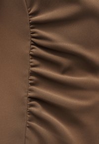 Καφέ ύφασμα με κάθετη ραφή και ρυτιδώσεις που δημιουργούν απαλά, ομοιόμορφα τοποθετημένες πτυχώσεις στη μία πλευρά, ενώ η άλλη πλευρά είναι λεία.