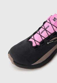 Svart og rosa treningssko med strukturert overflate, snøring og Gore-Tex-detalj. Designet inkluderer en konturert form og gummisåle.