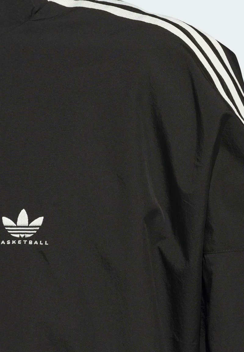 Schwarze Basketballjacke mit weißen Streifenakzenten, aus strukturiertem Stoff und mit gesticktem Logo auf der Brust.