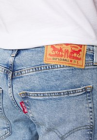Blue denim jeans with a faded finish, featuring a tan leather patch with red graphic details and a small red Levi's tag on the back pocket.