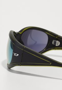 Mustad mustad prillid gradient objektiividega, läikiva viimistluse, roheliste aktsentide ja metallise logoga raamielementidega. Kumer ja sportlik disain.