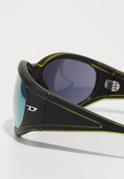 Lunettes de soleil noires avec des verres dégradés, dotées d'une finition brillante, d'accents verts et d'un logo métallique sur la monture. Design sportif et courbé.