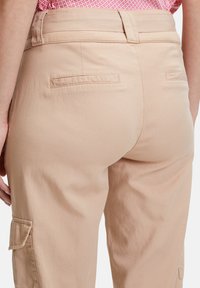 Beige Cargo-Hosen aus weichem Stoff, mit einem hinteren Bund mit Gürtelschlaufen, flachen Taschen und einer lässigen Passform mit seitlichen Cargotaschen.
