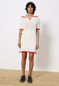 Strickkleid in Weiß mit roten Akzenten, mit V-Ausschnitt, kurzen Ärmeln und gewelltem Saum. Strukturiertes Material mit horizontalen Streifen.