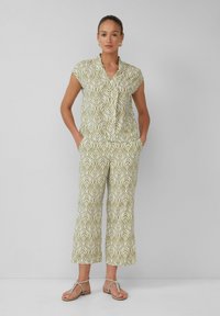 Zielony i biały kombinezon w wzory, z kołnierzykiem, krótkimi rękawami i szerokimi nogawkami. Posiada kieszenie boczne i gładką teksturę materiału.