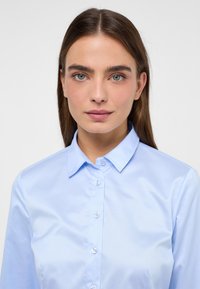 Camicia da uomo in cotone leggero blu chiaro, con colletto a punta, maniche lunghe e chiusura a bottoni. Tessuto liscio e vestibilità su misura.