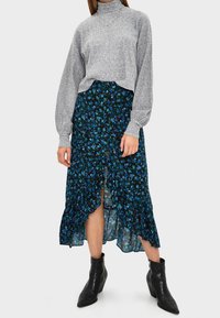 Pull à col roulé gris côtelé associé à une jupe fleurie bleu foncé avec des volants et une fente latérale, complété par des bottines noires.