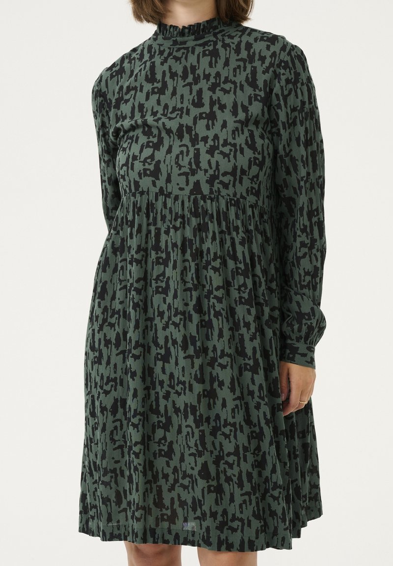 Langärmliges Kleid aus olivgrünem Stoff mit einem schwarzen abstrakten Muster, einem gerafften Ausschnitt und einer gedrapierten Taille für Volumen.