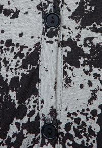 Černá a šedá látka s texturovaným vzhledem a vzorem, uprostřed léga se dvěma černými plastovými knoflíky.