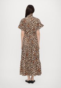 Maxikjole med leopardprint, korte volangermer, innsnørt midje og lagdelt skjørt. Båret med svarte flate sko, sett bakfra.