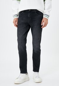 Jeans de mezclilla negra con corte recto, con un ligero desvanecimiento, diseño de cinco bolsillos y combinados con zapatillas blancas.