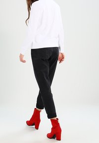 Felpa bianca, jeans di denim neri e stivaletti alla caviglia in suede rosso con tacco spesso. Dettaglio della cerniera visibile sugli stivaletti, gamba dei pantaloni cropped.