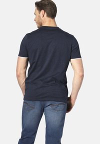 Marineblaues Kurzarm-T-Shirt mit Rundhalsausschnitt. Mit weißen Akzenten an den Ärmeln. Getragen mit hellblauen Jeans, die eine lässige Passform zeigen.