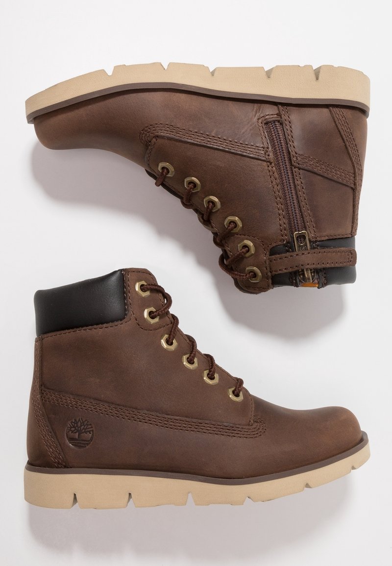 Bottes chevilles en cuir marron avec un col noir matelassé, des œillets dorés, une fermeture éclair latérale et des semelles en caoutchouc beige avec une bande de roulement antidérapante.