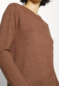 Brun stickad tröja med rund halsringning och långa ärmar. Mjuk textur och ett enfärgat mönster. Inga synliga dekorationer eller beslag.