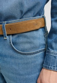 Blauwe spijkerbroek van denim met een lichte wassing, voorzien van een bruine suède riem met geperst "Lee." Details omvatten stiksels en een voorzak.