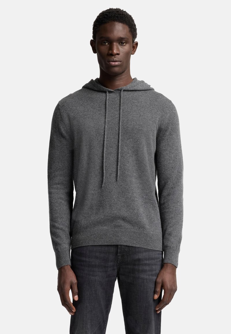 Grauer Kapuzenpullover mit strukturiertem Strick, langen Ärmeln und Kordelzug. Kombiniert mit dunklen Jeans.