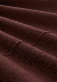 Tissu marron avec une surface douce et texturée, présentant des plis délicats et un motif de tissage subtil. Points de couture à peine visibles en accent.