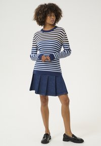 Námornícky modrý a krémový pruhovaný pletený sveter s rebrovanými manžetami, v kombinácii s tmavomodrou plisovanou sukňou. Čierne poltopánky dotvárajú outfit.