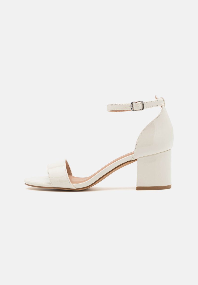 Hvit patentlær blokk-hæl sandal med ankelrem, åpen tå og glatt tekstur; har en sikker spenne og minimalistisk design.