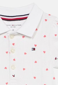 Λευκό βαμβακερό πόλο πουκάμισο με μικρό μοτίβο κόκκινων καρδιών, τρία κουμπιά και λογότυπο Tommy Hilfiger στο στήθος και στην εσωτερική ράχη του γιακά.