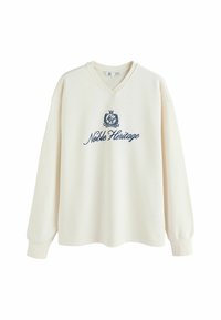 Sweatshirt crem cu decolteu în V, mâneci lungi, �și textul "Moștenire Nobiliară" brodat în nuanță de bleumarin. Material moale, cu un croi lejer.