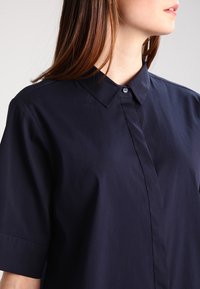Marinblå kortärmad skjorta med knäppkrage, som har en slät, matt yta och en diskret lyster i tyget.