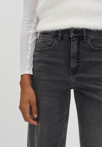 Jeans in denim nera con un design aderente, caratterizzati da tasche anteriori e una leggera texture sfrangiata. Abbinati a un top bianco a maniche lunghe.