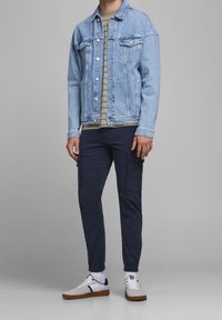 Ljusblå denimjacka över en grårandig skjorta, ihop med mörka cargobyxor och vita sneakers med bruna accenter.