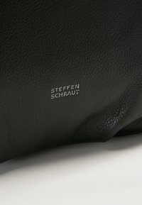 Surface en cuir noir texturé avec un petit texte blanc "Steffen Schraut" centré dessus, reposant sur un fond clair.