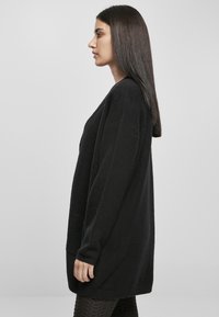 Black, textured cardigan with a relaxed fit, long sleeves, and side pockets, showcased from a side view against a neutral background.