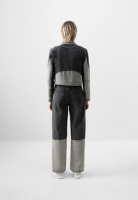 Chaqueta de mezclilla y pantalones en tonos negros y grises. La chaqueta tiene un diseño corto; los pantalones tienen piernas anchas con paneles inferiores en contraste.