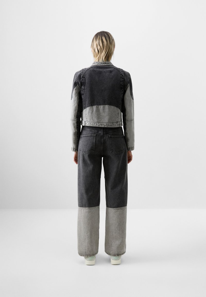 Giubbotto di jeans e pantaloni in tonalità di nero e grigio. Il giubbotto presenta un design corto; i pantaloni hanno gambe larghe con pannelli inferiori a contrasto.