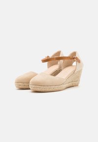Zapatos de cuña tipo espadrille beige con una parte superior de suave gamuza, tira ajustable marrón y media suela de yute trenzado. Diseño de puntera cerrada, detalles texturizados.
