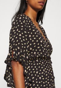 Schwarzes Blumenkleid mit tiefem V-Ausschnitt, kurzen Volantärmeln und kleinen rosa und gelben Blumenmustern auf dem Stoff.